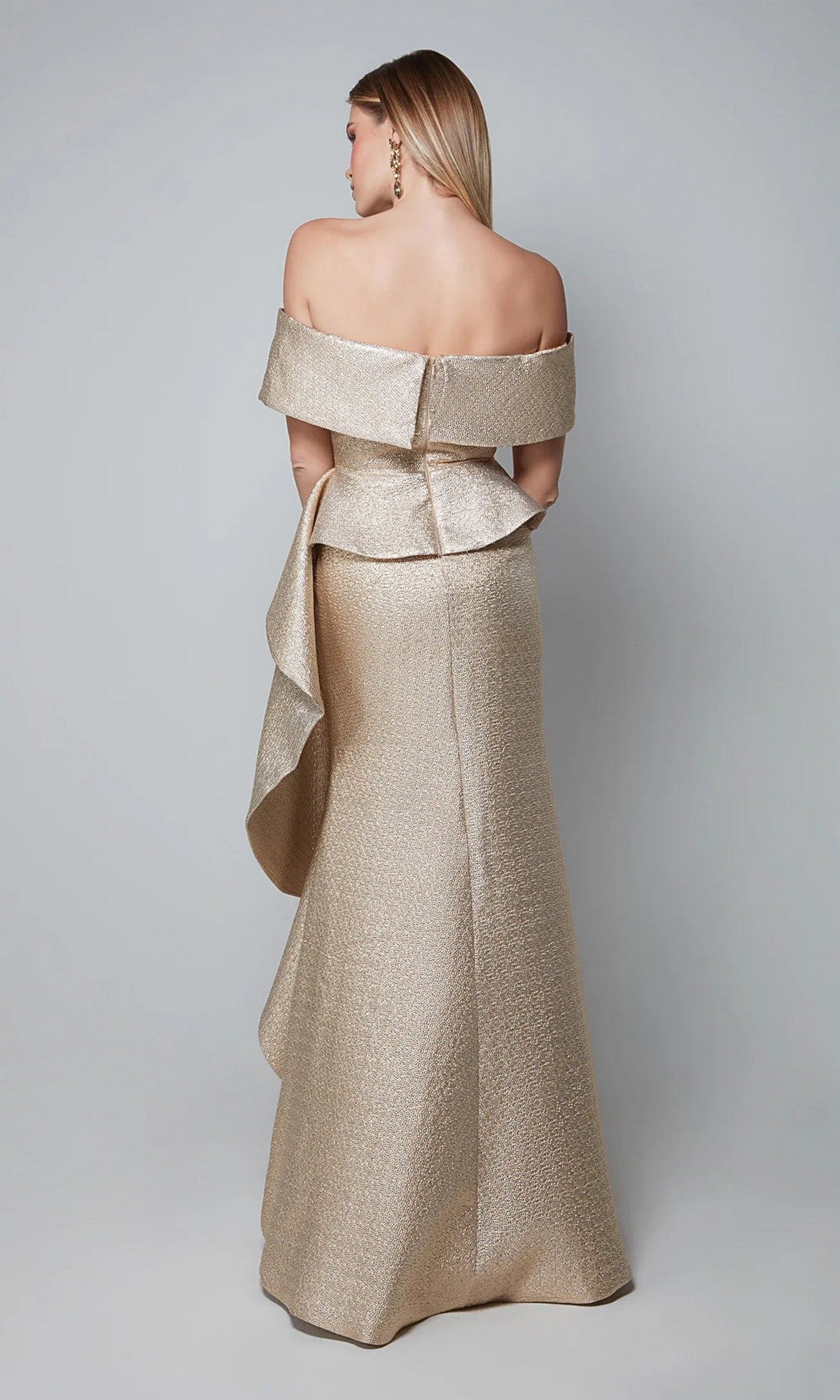 A woman faces away, wearing the Alyce 27612 long formal dress—a metallic gold, floor-length gown with an off-the-shoulder neckline and ruffled side detail.